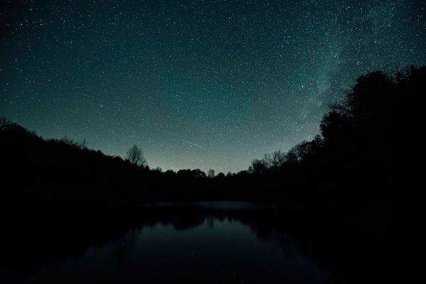 Starry night sky reflecting on a calm lake surrounded by silhouettes of trees. Espace 4K