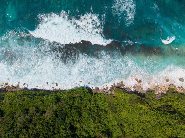 Stunning aerial view of Bali's coastline featuring turquoise waves and lush green vegetation. Nature 4K