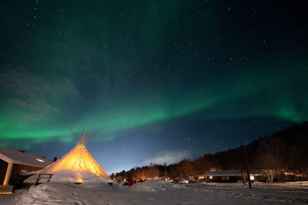 Stunning aurora borealis over a snowy landscape with a lit teepee near Alta, Norway. Espace 4K