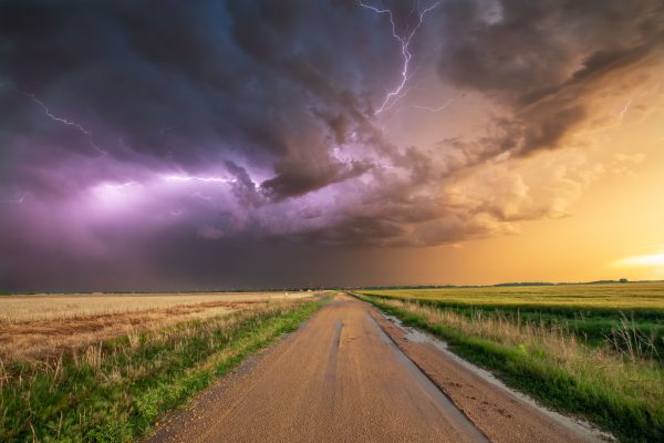 Stunning photo of a thunderstorm with lightning over a wheat field and dirt road in Oklahoma. Dark 4K
