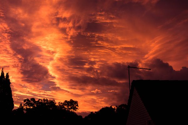 Stunning sunset sky with clouds in vibrant orange hues and silhouette of trees and a rooftop antenna. Dark 4K