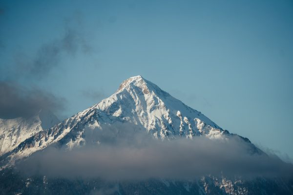 Stunning view of a snow-covered mountain peak emerging from clouds under a clear blue sky. Nature 4K