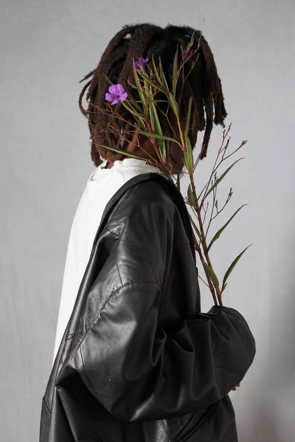 Stylish person in black jacket holding purple flowers against neutral background. Mobile 4K