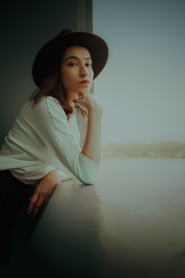 Stylish woman in a black hat and white shirt posing thoughtfully indoors. Mobile 4K