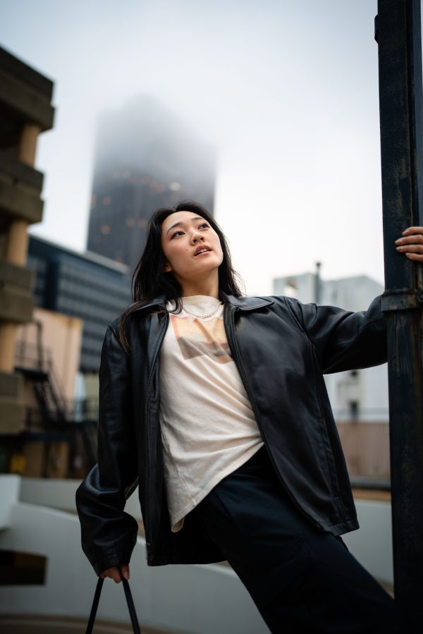Stylish woman in a leather jacket posing in a modern cityscape on a foggy day. Mobile 4K