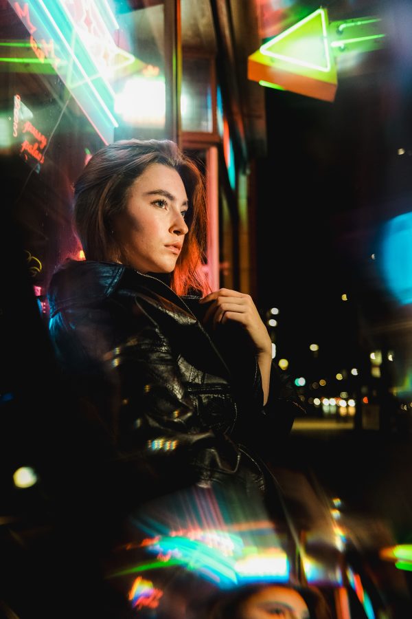 Stylish woman poses with neon reflections at night in urban setting. Mobile 4K
