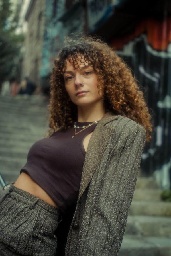 Stylish young woman with curly hair posing on urban stairs with graffiti background. Mobile 4K