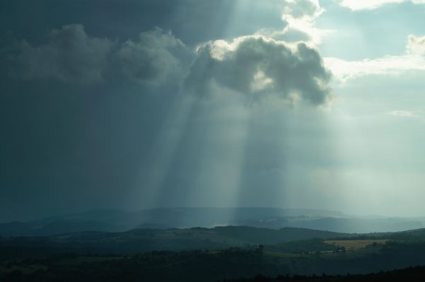 Sunbeams piercing through clouds over a serene countryside landscape at sunset. Dark 4K