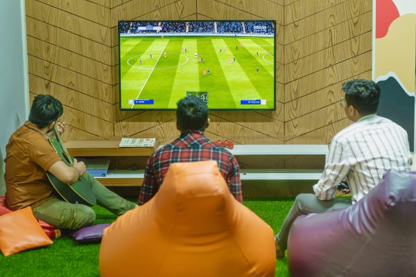 Three friends relaxing and playing a soccer video game indoors on a comfortable game night. Wallpaper 4K