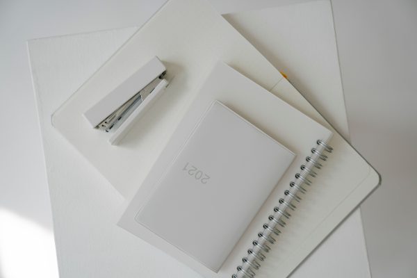 Top view of notebook and diary with white stapler located on opened planner with blank pages against white background Minimaliste 4K