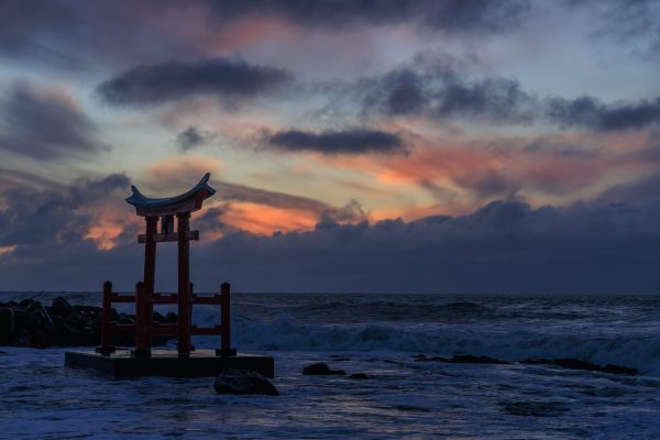 Torii gate silhouette against a stunning sunset sky over the waves in Shosambetsu, Hokkaido. Anime 4K