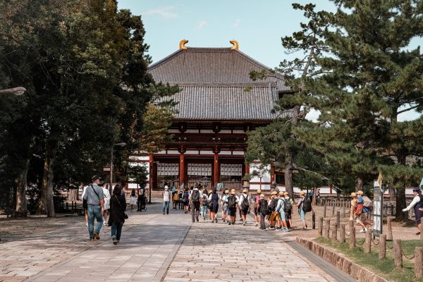 Tourists walking towards Todai-ji Temple in Nara, Japan, surrounded by trees and historical architecture. Anime 4K