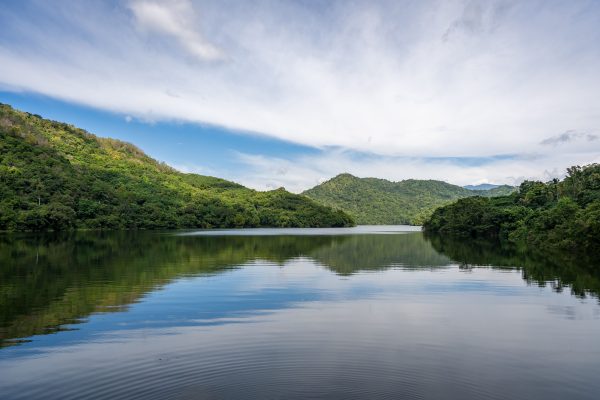 Tranquil lake surrounded by lush green hills under a bright blue sky. Perfect nature scene. Nature 4K