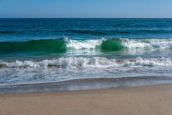 Tranquil ocean waves crash upon a sandy beach under a clear blue sky. Nature 4K