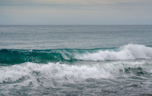 Tranquil view of ocean waves crashing onto the sandy shore under a calm cloudy sky. Nature 4K