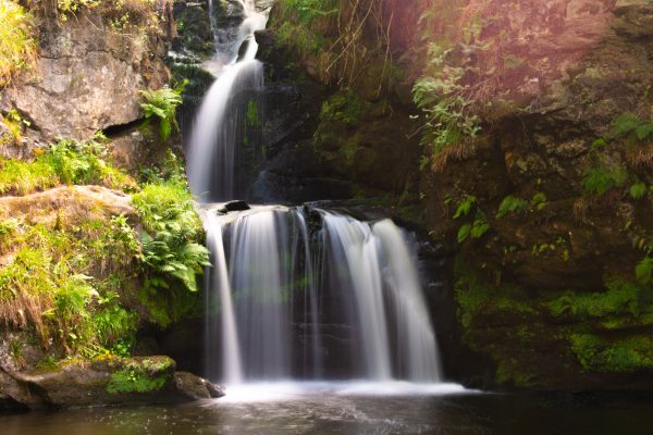 Tranquil waterfall amidst lush greenery and rocky terrain in Aberlour, Scotland. Nature 4K