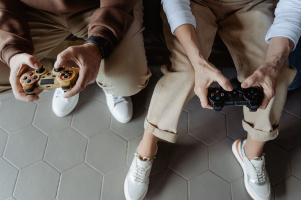 Two adults playing video games with controllers while seated on a sofa, having fun indoors. Gaming 4K