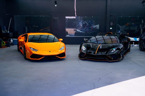 Two luxury sports cars, orange and black, parked in a stylish indoor garage. Voitures 4K
