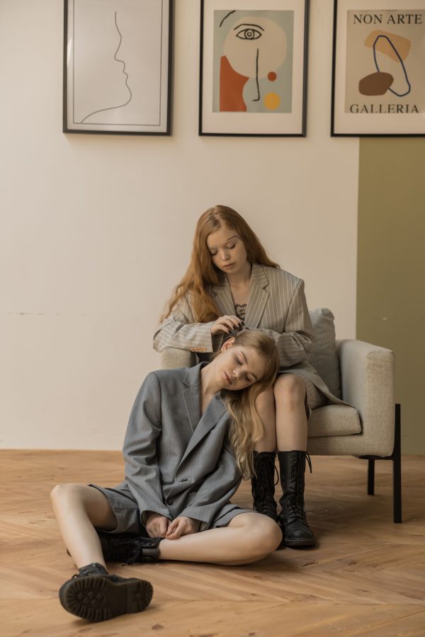 Two women in oversized blazers pose in a minimalist room with artistic decor. Mobile 4K