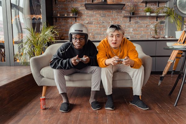 Two young men focused on video gaming indoors on a cozy sofa with controllers. Gaming 4K