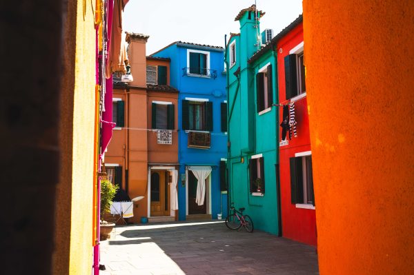 Vibrant alleyway with colorful houses in Burano, Venice illuminated by sunlight. Abstrait 4K