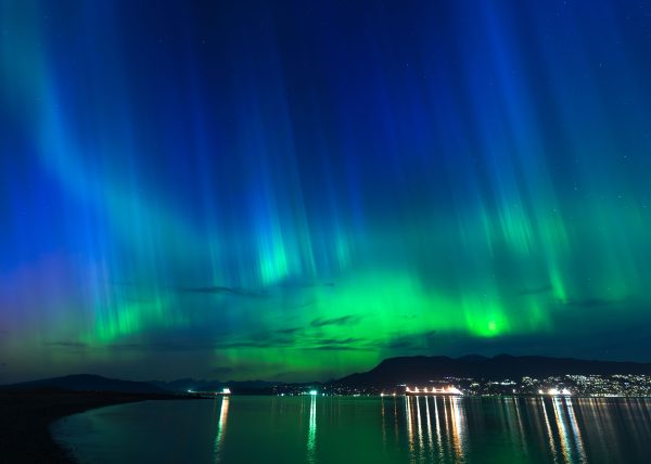 Vibrant aurora borealis illuminating the night sky above a city by the sea. Espace 4K