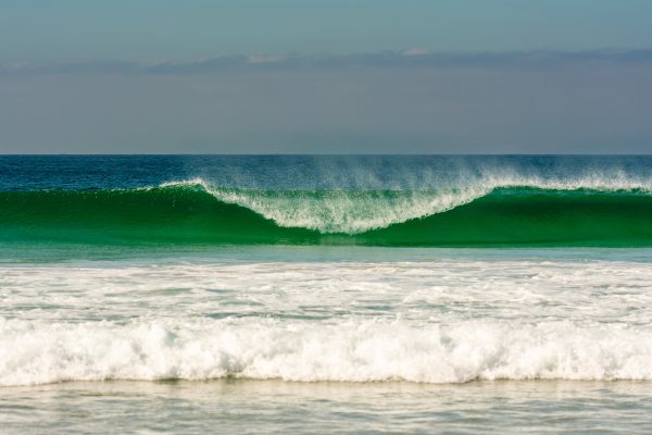 Vibrant ocean wave rolling towards a serene sandy beach under a clear sky. Nature 4K