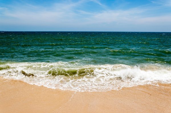 Vibrant ocean waves gently caress the sandy shore under a clear blue sky. Nature 4K