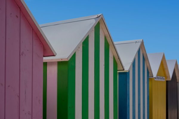 Vibrant striped beach huts under a clear blue sky, showcasing summer vibes. Abstrait 4K