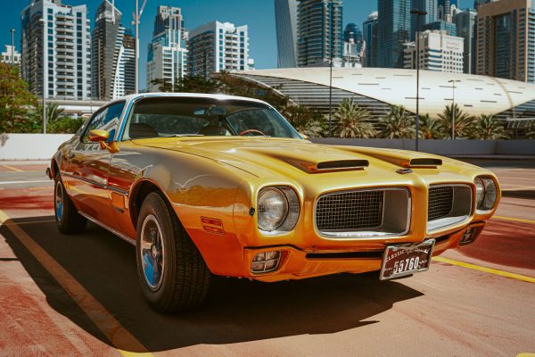 Vintage yellow Pontiac parked amidst Dubai's iconic skyline under sunny skies. Voitures 4K
