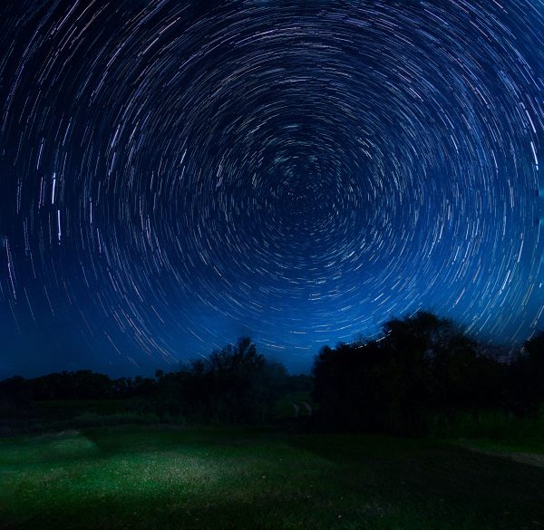 Vivid star trails creating a hypnotic pattern in a dark night sky over a tranquil outdoor landscape. Espace 4K