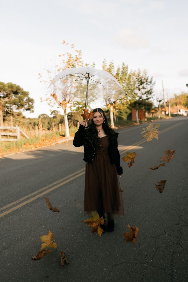 Woman holding an umbrella on a rural road with autumn leaves around her, conveying a serene fall scene. Mobile 4K
