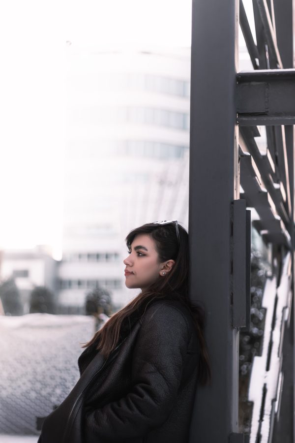 Woman in a winter puffer jacket leaning against a structure outdoors in Mashhad. Mobile 4K
