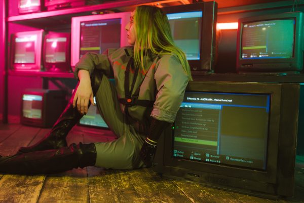 Woman in cyberpunk attire sits surrounded by vintage TVs in a neon-lit room, evoking retro-futuristic vibes. IA Générative 4K