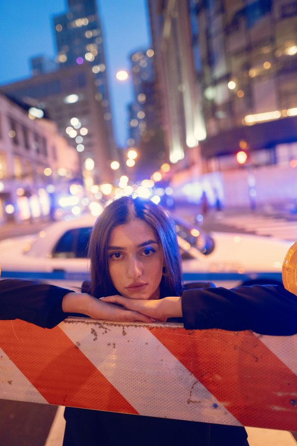 Woman leaning on barricade with city lights and urban buildings at night. Mobile 4K