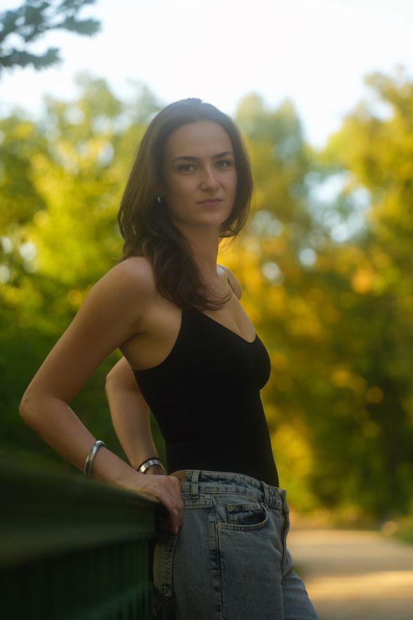 Woman posing outdoors with autumn trees in the background, wearing casual outfit. Mobile 4K