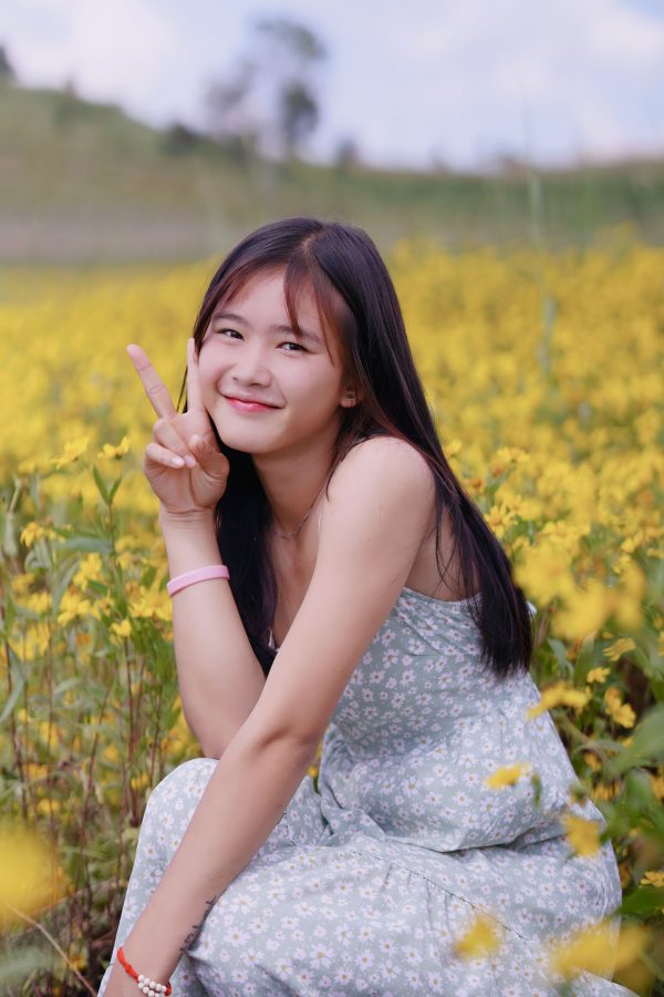 Woman posing with a peace sign in a vibrant yellow flower field, exuding a cheerful, sunny vibe. Mobile 4K