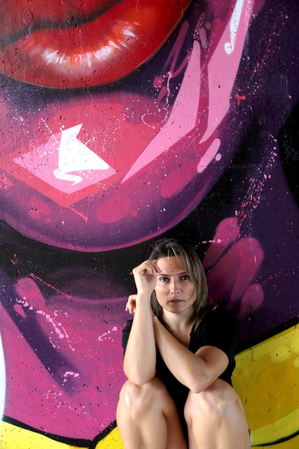 Woman sitting before a colorful graffiti mural, urban art exploration. Mobile 4K