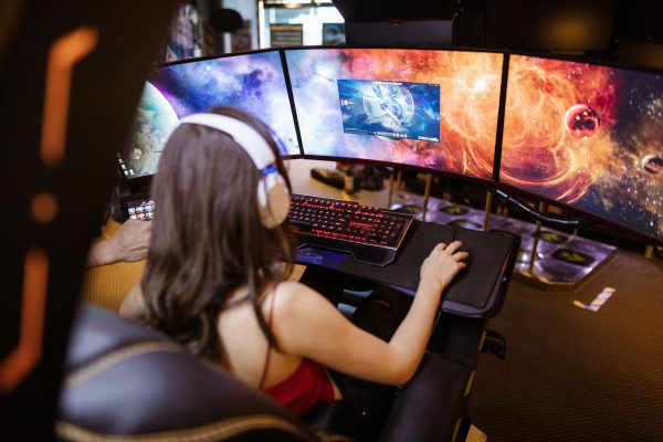 Woman with headphones playing on a multi-screen gaming setup featuring vibrant space imagery. Gaming 4K