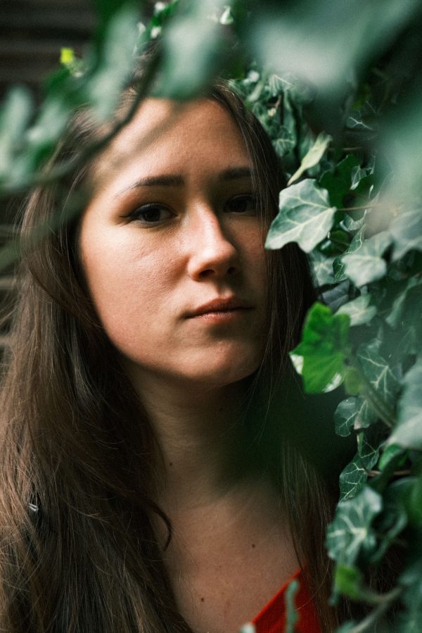 Woman with long brown hair posing with green leaves. Natural light creates a serene atmosphere. Mobile 4K