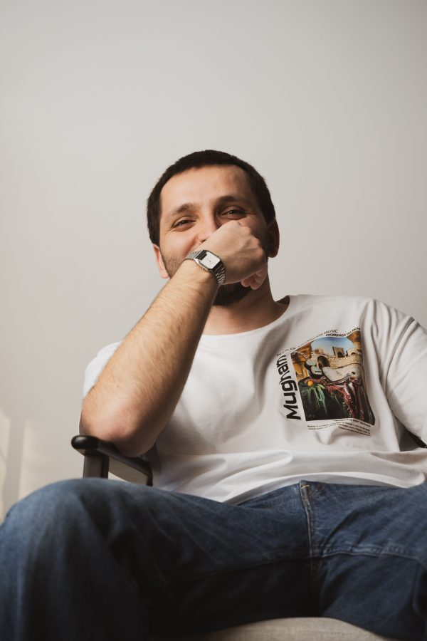 Young man sitting casually in a chair, wearing a printed T-shirt and jeans, with a relaxed expression. Mobile 4K