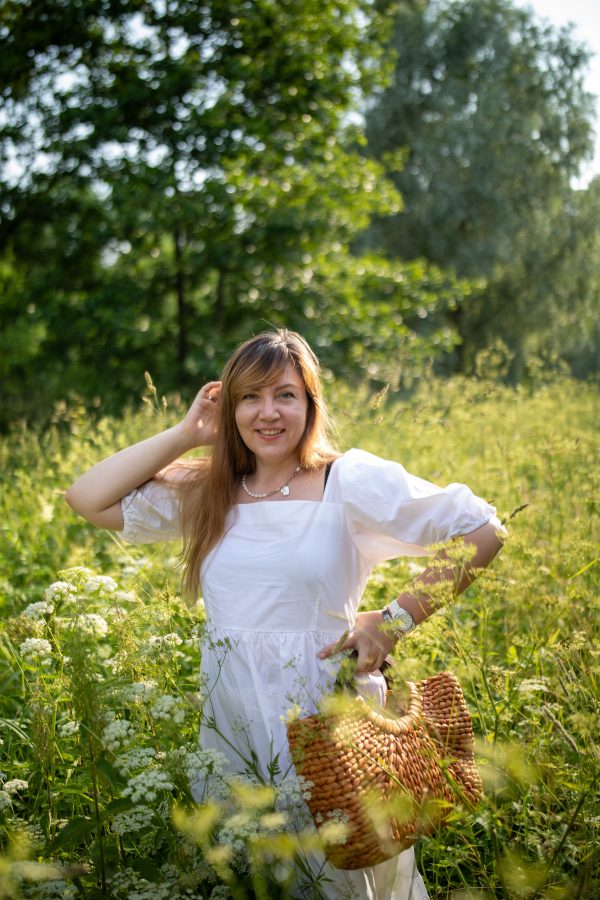 Young woman in a white dress smiling in a sunlit summer meadow with wildflowers. Mobile 4K