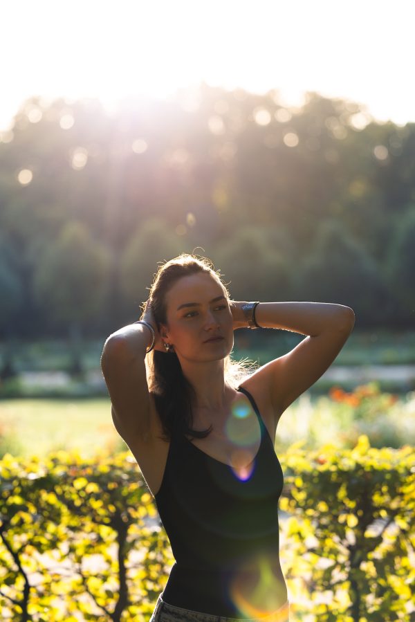 Young woman posing in a sunlit garden with hands in hair, creating a dreamy summer ambiance. Mobile 4K